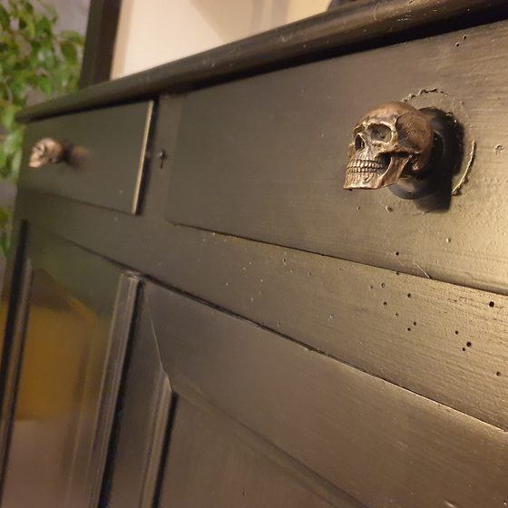 A bronze-finish skull knob fitted to a wooden dresser drawer